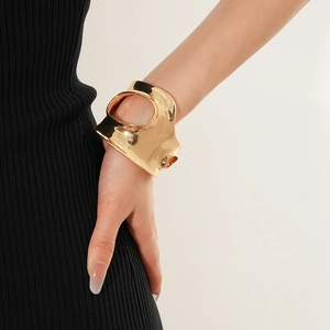 Gros plan d'un large bracelet manchette doré irrégulier porté au poignet d'un modèle