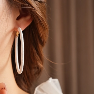 Close-up of white leather geometric hoop earring with gold pin worn by a model