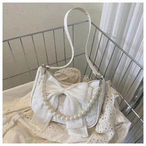 Detail of white lace handbag featuring decorative bow and elegant pearl handle