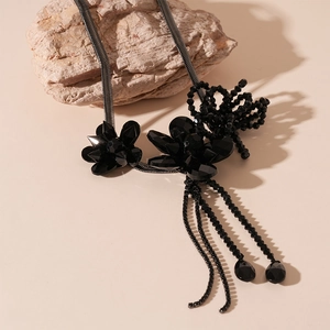 Detail of dark gothic floral pendant with bead tassels and black snake chain on rock