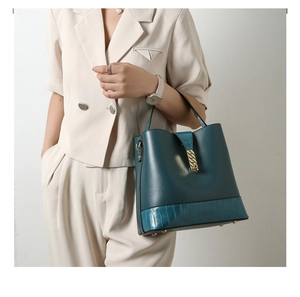 Detail of dark teal bucket bag featuring textured leather panels and gold chain lock hardware