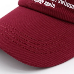 Detailed close-up of burgundy cotton baseball cap with white embroidery and stitching