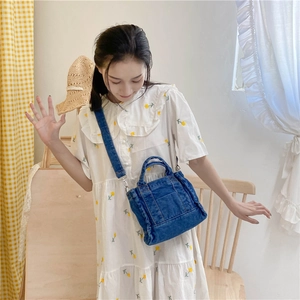 Detail of blue denim tote bag with raw edges and silver hardware shown in lifestyle setting