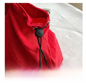 Detail of red drawstring bag showing metal eyelet, black cord and adjustable toggle