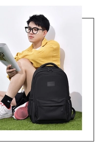 Black nylon backpack shown on a model sitting in a park setting for casual lifestyle look