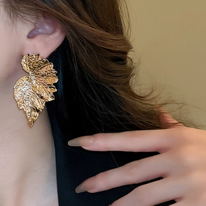 Macro detail of a large golden leaf earring with textured veins worn by a model