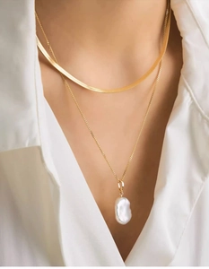 Detail of layered gold snake chain and natural baroque pearl pendant on woman neck