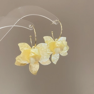 Détail de boucles d'oreilles fleurs en résine jaune avec crochets dorés sur support