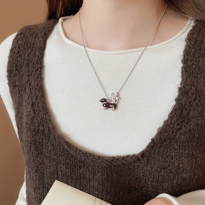 Gros plan d'un collier avec pendentif teckel en argent porté sur un gilet en maille