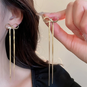 Close-up of elegant gold bow earrings with long fringe tassels worn for a luxury style