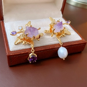 Close-up of asymmetric gold earrings with baroque pearl, amethyst and zircon leaf details
