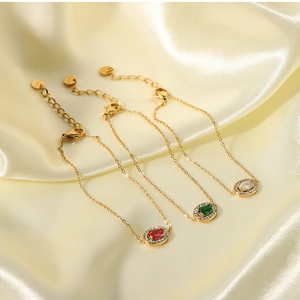 Three gold stainless steel bracelets with red, green, and white oval zircon stones on silk