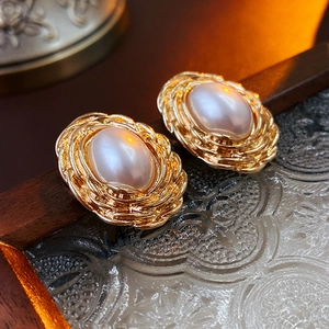 Close-up of vintage oval pearl earrings with elegant gold braided metal frames