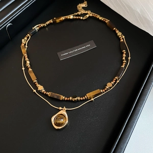 Detail of layered gold necklace with brown tiger eye beads and geometric stone pendant