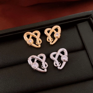 Macro shot of gold and silver snake-shaped heart earrings with zircon studs