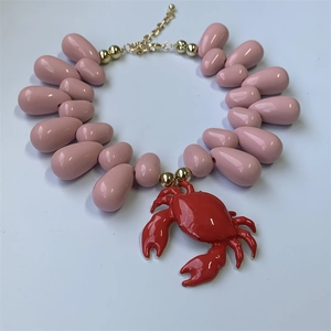 Detail of nautical necklace with pink teardrop beads and a red crab pendant on white