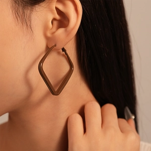 Detailed close-up of a model wearing brown matte geometric square hoop earrings