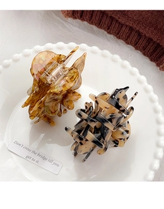 Detail view of acetate flower hair claws in amber and tortoiseshell on a ceramic tray