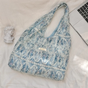 Close-up of light blue lace tote bag with floral embroidery and gold metal plaque