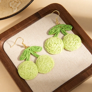 Macro detail of handmade raffia cherry fruit earrings with green leaves and metal hooks