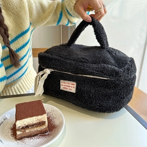 Detail of black plush makeup bag featuring white ribbon and elegant label in a cafe setting