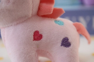 Close-up of pink plush unicorn with colorful heart embroidery and soft fabric texture