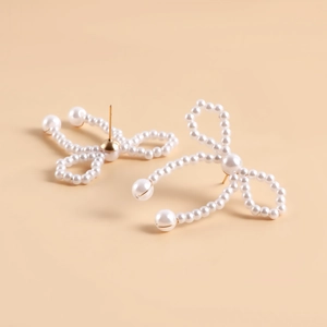 Detailed view of handmade pearl bow earrings with golden metal studs on beige background