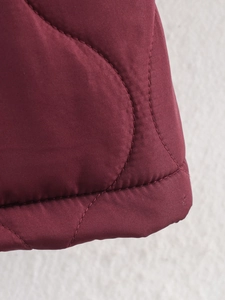 Close-up of wine red quilted coat detailing stitched hem and polyester fabric texture