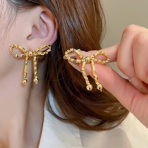 Vue détaillée des boucles d'oreilles nœud en métal doré avec pompons et perles en cascade