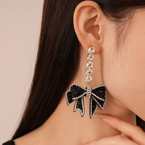 Close-up of elegant black and gold bow earrings with sparkling rhinestones on model