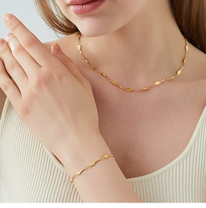 Detail of a gold tennis racket necklace and bracelet set worn on a model in sunlight