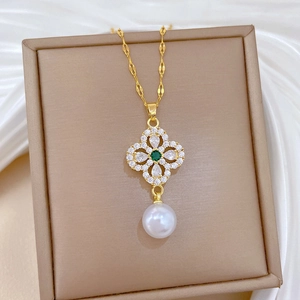 Macro shot of gold four-leaf clover pendant with green stone and white pearl detail