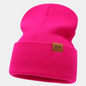 Detail of rose red knit beanie featuring a brown leather Mom patch with ribbed texture