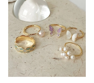 Detailed close-up of gold butterfly rings with pearls and enamel on textured beige paper