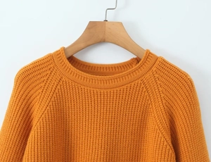 Détail d'un pull en maille orange montrant la texture épaisse et le col rond sur un cintre