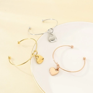 Detailed view of polished heart charm open bangles in gold, silver, and rose gold finish