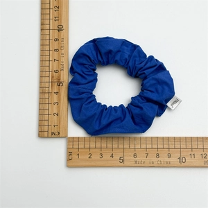 Close-up measurement of blue cotton scrunchie showing outer diameter and brand tag