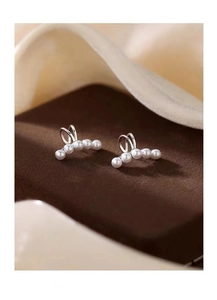 Macro shot of 925 silver plated ear cuffs with five delicate pearls on soft fabric