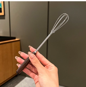 Close-up of a mini stainless steel whisk with ergonomic dark brown wooden handle