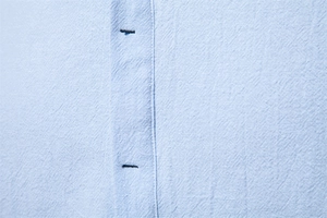 Macro shot of light blue cotton linen fabric texture with stitching and buttonhole details