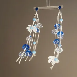 Macro shot of long floral tassel earrings with blue beads on a transparent display stand
