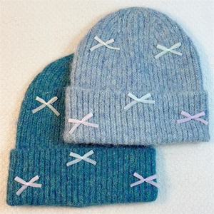 Sweet knit beanies with ribbon bows in light blue and teal on white textured fabric