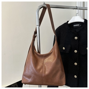 Detail of brown PU leather tote bag hanging against a black tweed jacket background
