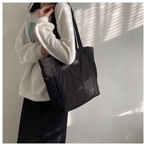 Model view of large black nylon tote bag against minimalist wall with natural lighting