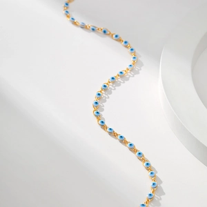 Detail of 18K gold-plated evil eye chain with blue glass beads on white stone base