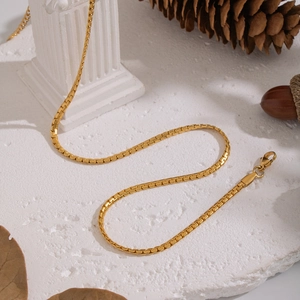 Golden minimalist chain necklace displayed on a textured pedestal with classic decor