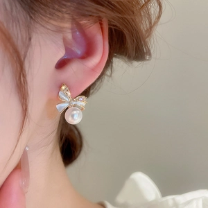 Close-up of bow earrings with shimmering zircons and an elegant white pearl drop