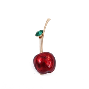Close-up of a red cherry brooch with golden stem and green crystal leaf detail
