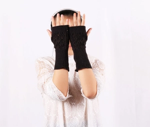 Detail of black knitted fingerless long gloves featuring an intricate hollow leaf pattern