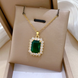 Macro detail of gold necklace with emerald green square pendant and diamond accents